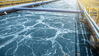 Pipes and a reservoir of blue, foamy water at a wastewater treatment plant